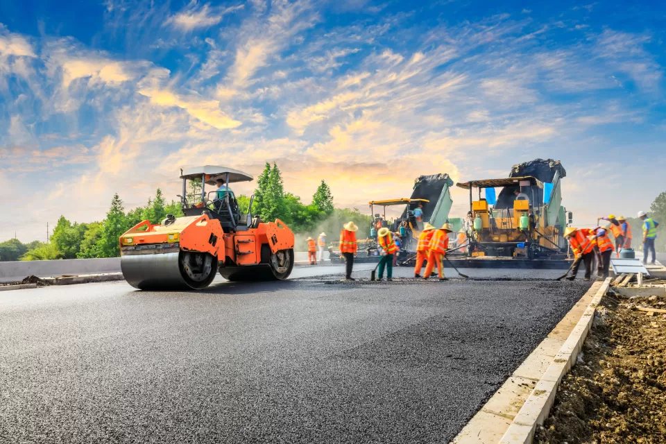 Crew in orange safety vests stand on roadway next to orange heavy equipment
